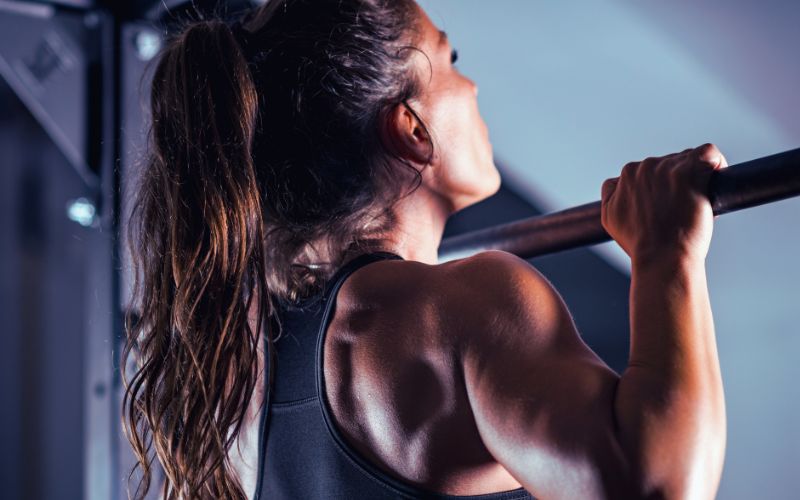 A woman in sportswear does a pull-up in a gym in Melbourne’s west, highlighting strength and recovery like remedial massage.