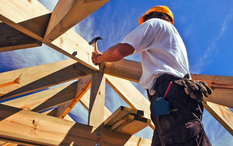 A construction worker in Melbourne’s west, Brooklyn, builds a roof frame under a blue sky—like remedial massage supporting you.