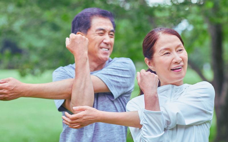 Two adults smiling as they stretch outdoors among green trees in Brooklyn, Melbourne’s west, promoting remedial massage and wellbeing.