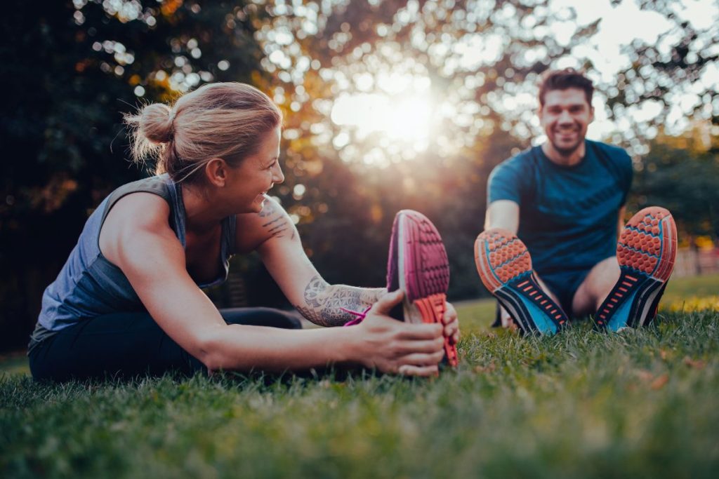 Two people relax on grass in Brooklyn, Melbourne’s west, stretching and smiling after a sports massage session outdoors.