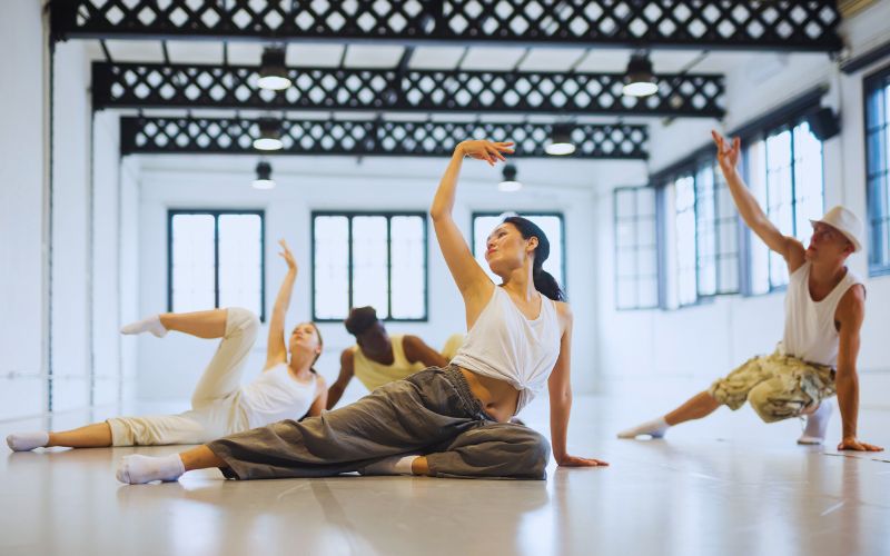 Four dancers in casual outfits pose on the floor of a bright Brooklyn studio, ideal for West Melbourne dance recovery such as dry needling.